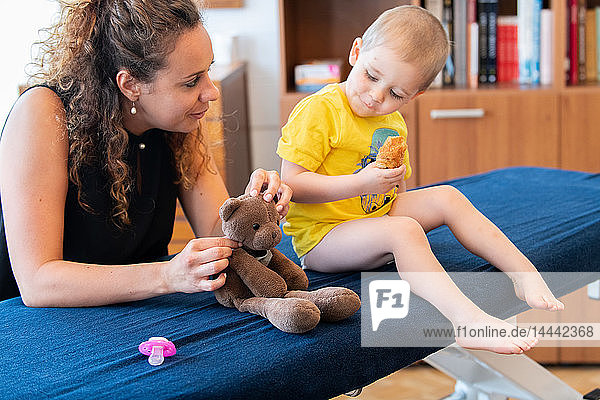 Osteopathische Konsultation bei einem Kind: das Vertrauen des Kindes gewinnen  indem die Manipulation am Spielzeug des Kindes nachgeahmt wird.