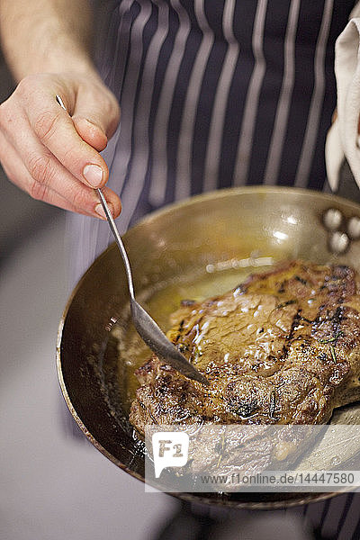 Steak being basted with butter in a pan