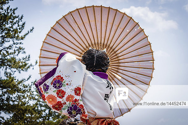 Japanisches Mädchen trägt traditionellen Regenschirm während eines Frühlingsfestes.