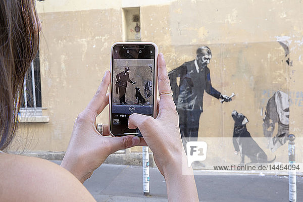 Close-up of hands taking pictures of Bansky's work with a mobile phone. Street Victor Cousin. June 21  2018. Paris  French.