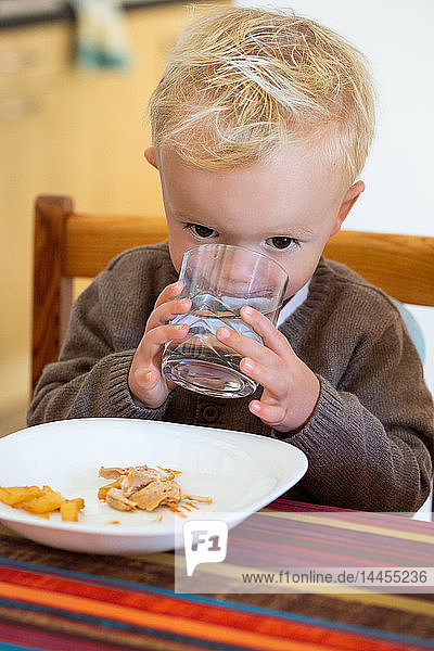 Portrait of a little boy drinking a glass of water during the meal.