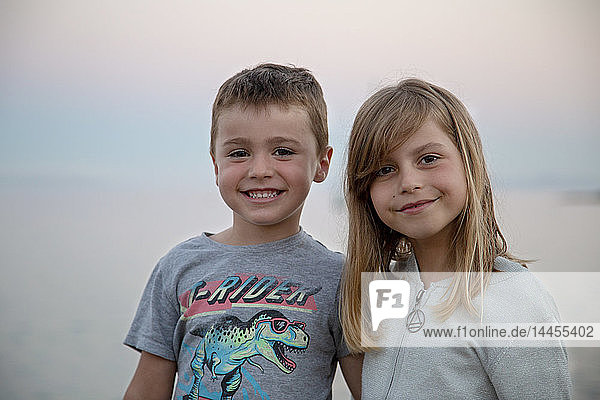 Ein kleines Mädchen und ihr Bruder posieren zärtlich vor dem Meer bei Einbruch der Dunkelheit.