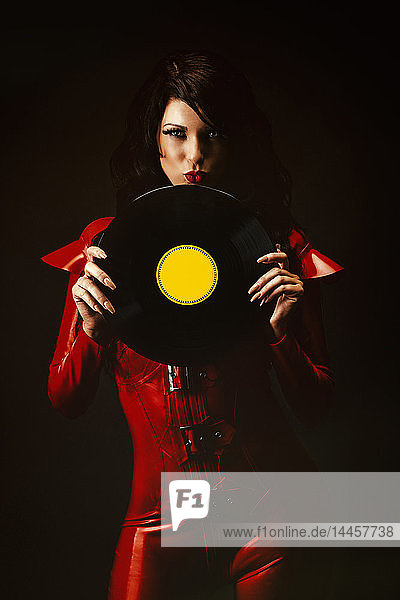 Portrait of a sexy young woman in red latex overall  a vinyl record in her hands