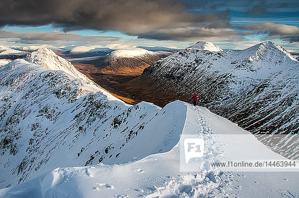 Eine Wanderin nähert sich dem Gipfel des Stob Dubh auf Buchaille Etive Beag an einem klaren Wintertag  Highlands  Schottland  Vereinigtes Königreich