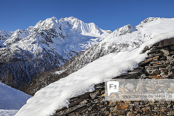 Stone hut covered with snow with Monte Disgrazia on background Alpe dell'Oro Valmalenco Valtellina Lombardy Italy