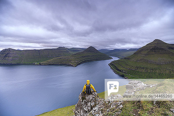 Wanderer auf Felsen sitzend mit Blick auf die Fjorde  Funningur  Insel Eysturoy  Färöer Inseln  Dänemark