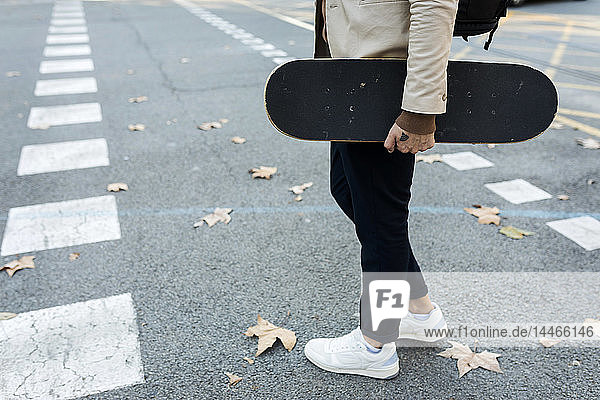 Mann mit Rucksack und Skateboard beim Überqueren der Straße im Herbst  Teilansicht