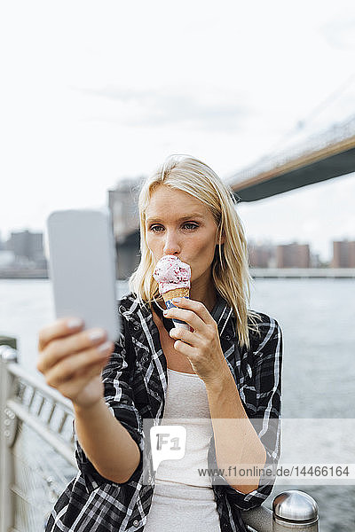 USA  New York City  Brooklyn  junge Frau  die am Wasser steht  ein Eis isst und ein Selfie nimmt