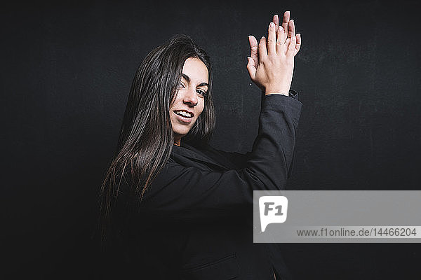 Porträt einer lächelnden jungen Frau  die vor schwarzem Hintergrund in die Hand klatscht