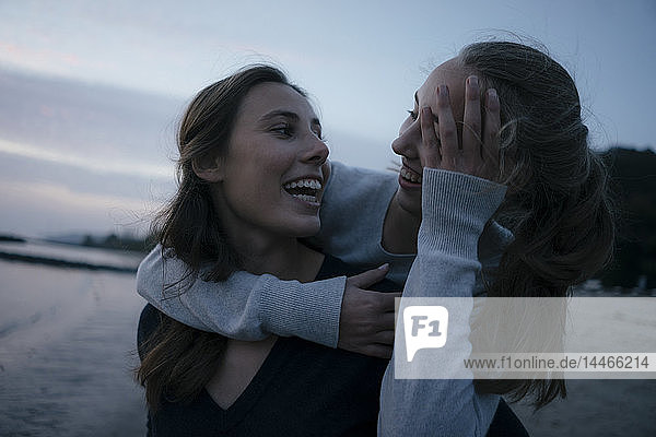 Deutschland  Hamburg  zwei fröhliche Teenager-Mädchen  die sich abends am Strand am Elbufer umarmen