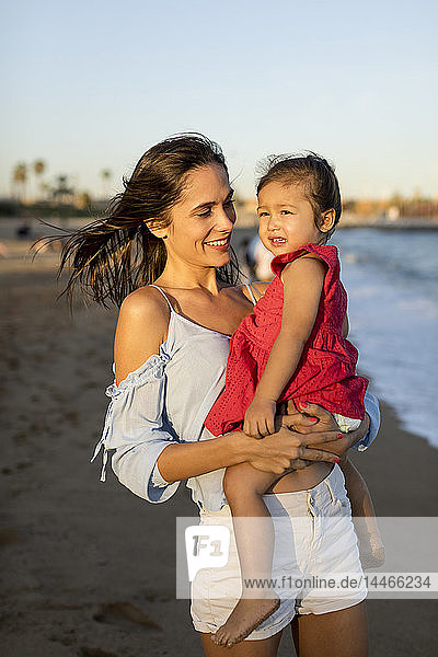 Mother and daughter standing on the beach at sunset
