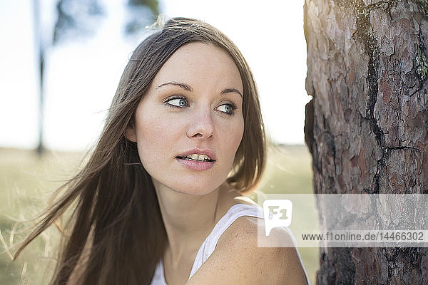 Porträt einer jungen Frau  die sich an einen Baumstamm lehnt