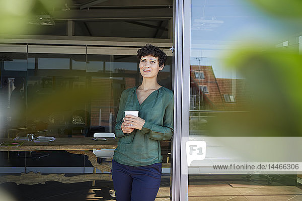 Lächelnde Frau steht am Fenster und macht eine Kaffeepause
