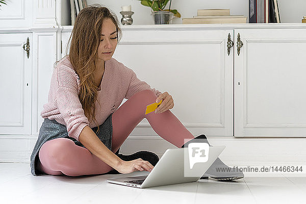 Young woman sittiing on the floor  doing an online payment with her credit card