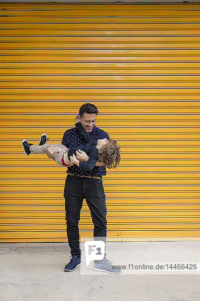 Glücklicher Vater trägt Sohn am gelben Rollladen