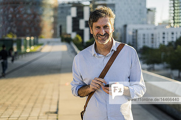 Porträt eines lächelnden reifen Mannes mit Handy in der Stadt