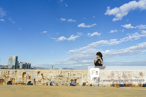 Spanien  Barcelona  Frau mit Smartphone und Kaffee zum Sitzen an der Wand