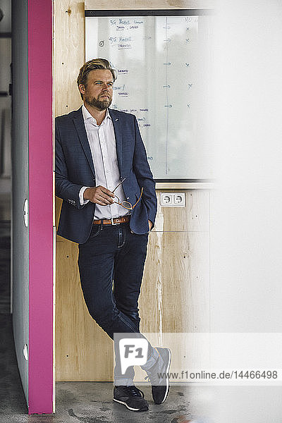 Businessman standing in office  holding glasses  leaning on white board