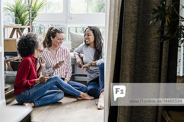 Drei glückliche Frauen sitzen zu Hause mit Mobiltelefonen auf dem Boden