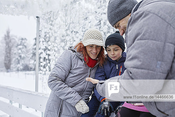 Familie mit zwei Kindern auf der Eisbahn  die sich Selfs auf ihrem Smartphone anschauen