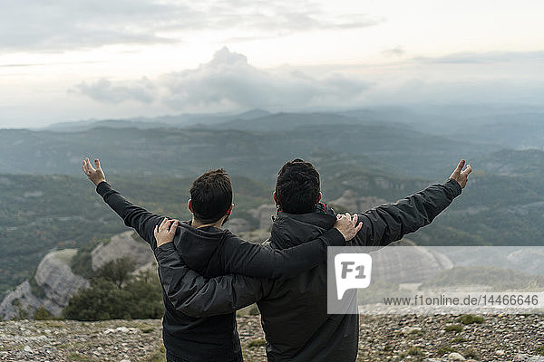 friends standing on mountain peak with arms around  enjoying he view
