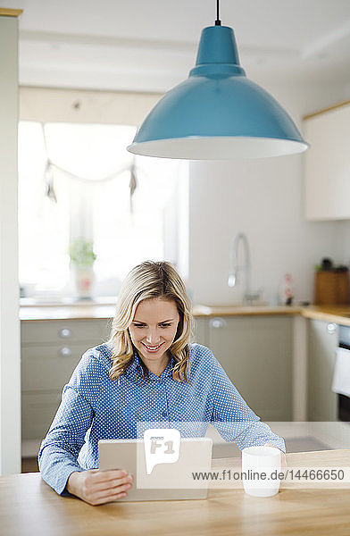 Lächelnde Frau mit Tablette zu Hause am Tisch sitzend