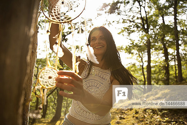 Happy woman hanging dream catcher on a tree