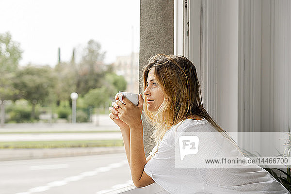 Junge Frau am Fenster mit einer Tasse Kaffee in der Hand