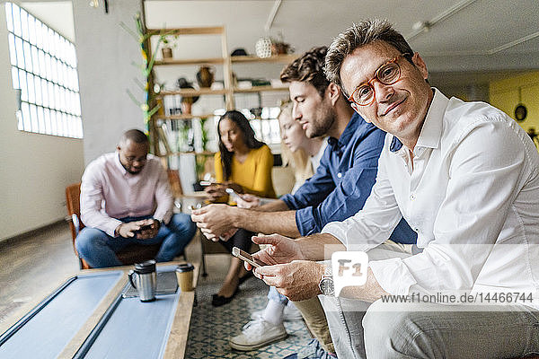 Business team sitting in loft office using cell phones