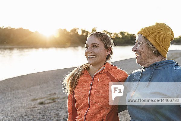Fit grandmother and granddaughter walking at the river with arms around  having fun