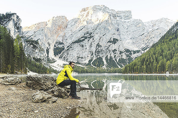 Italien  Pragser Wildsee  Mann sitzt auf einem Felsen am Seeufer mit Bergen und Wald im Hintergrund