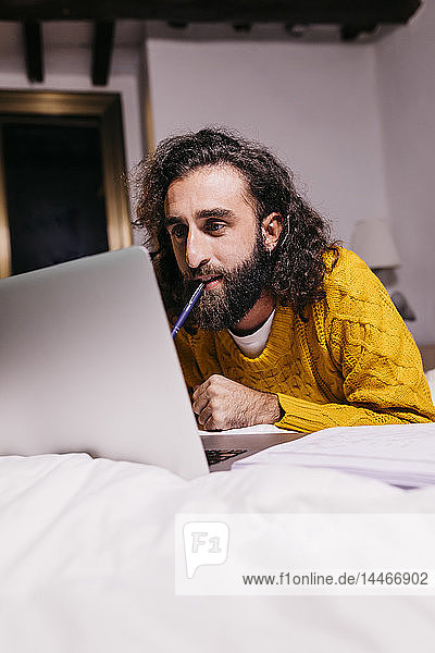 Junger Mann liegt zu Hause mit Laptop im Bett