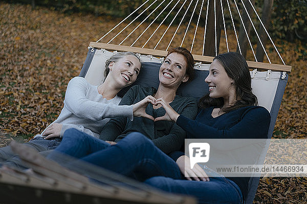 Glückliche Mutter mit zwei Mädchen im Teenageralter  die im Herbst in der Hängematte im Garten liegen