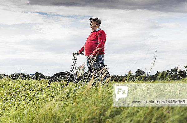 Älterer Mann mit Fahrrad in ländlicher Landschaft