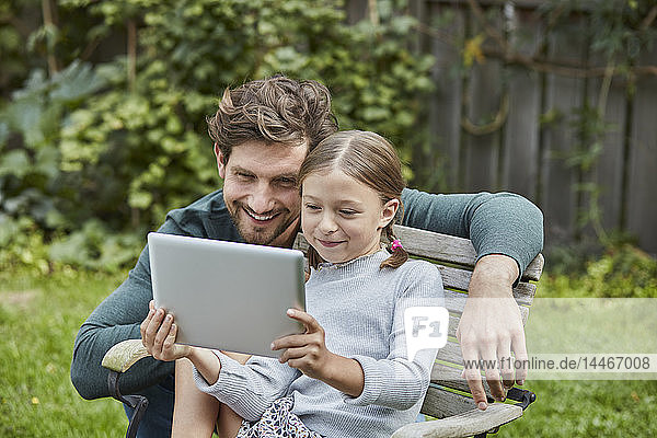 Glücklicher Vater und Tochter benutzen gemeinsam Tablette im Garten