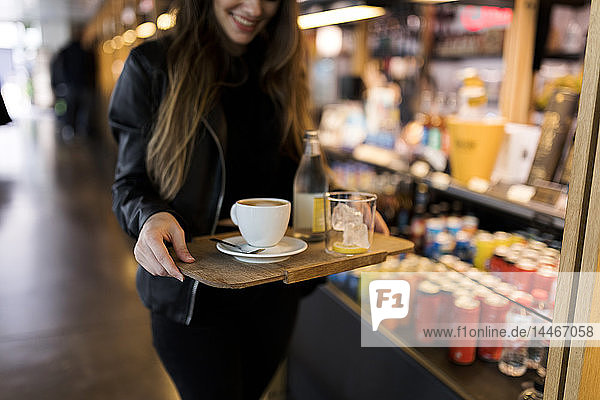 Close-up of woman carrying tray with coffee and soft drink in a self service cafe