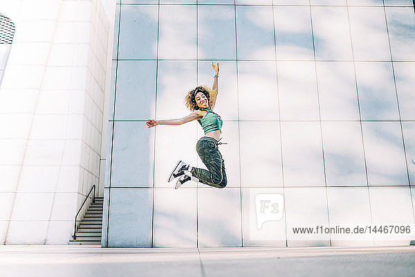 Portrait of happy young woman jumping at a building