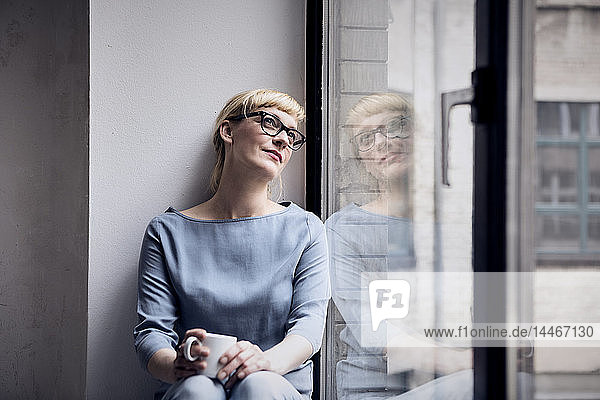 Porträt einer lächelnden Frau mit Kaffeetasse beim Blick durchs Fenster