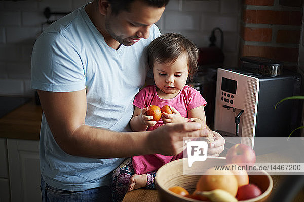 Father and baby girl eating fruit in kitchen at home
