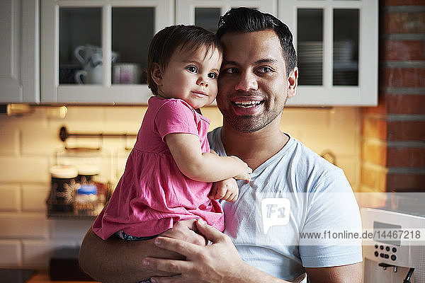 Smiling father holding baby girl in kitchen at home