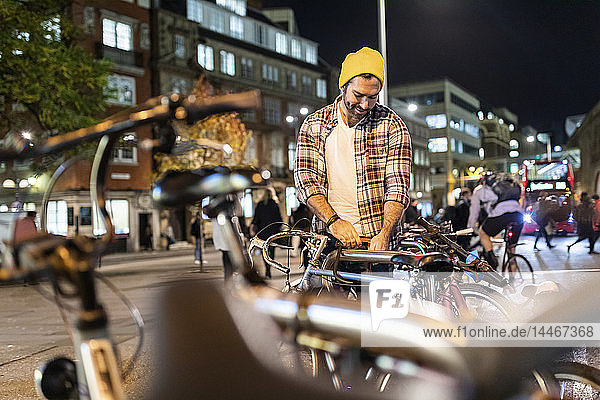 UK  London  man unlocking his bike and commuting at night in the city