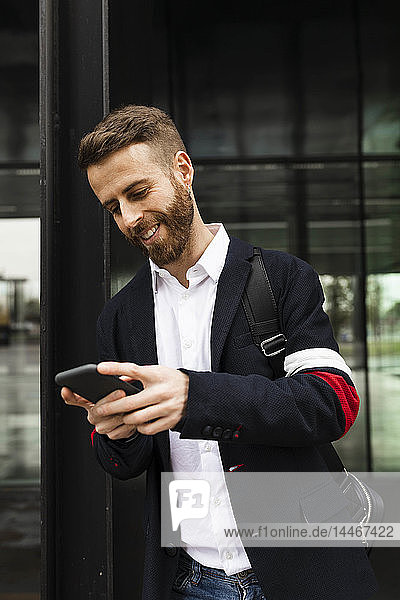 Lächelnder stilvoller Geschäftsmann mit Handy in der Stadt