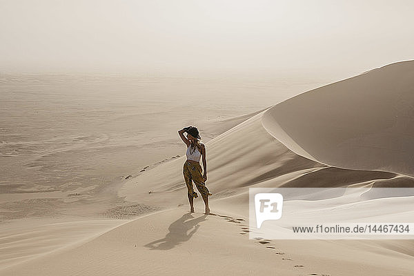 Namibia  Namib  Frau steht auf einer Wüstendüne und schaut auf die Aussicht