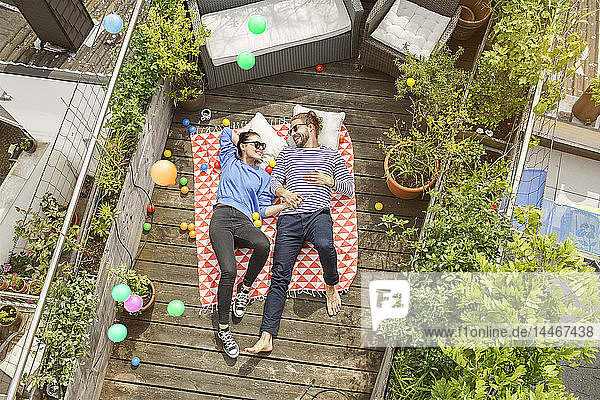 Junges Paar entspannt sich auf dem Balkon  auf einer Decke liegend und die Arme um den Körper gelegt