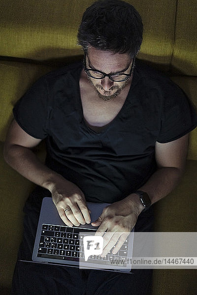 Man sitting on couch using laptop at night