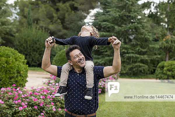 Happy father carrying son on shoulders in park