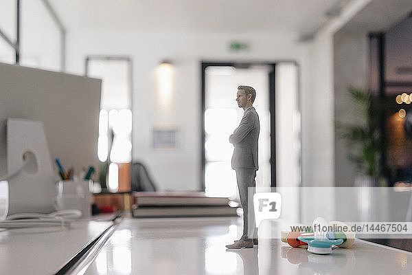 Businessman figurine standing on desk with pacifier and toys