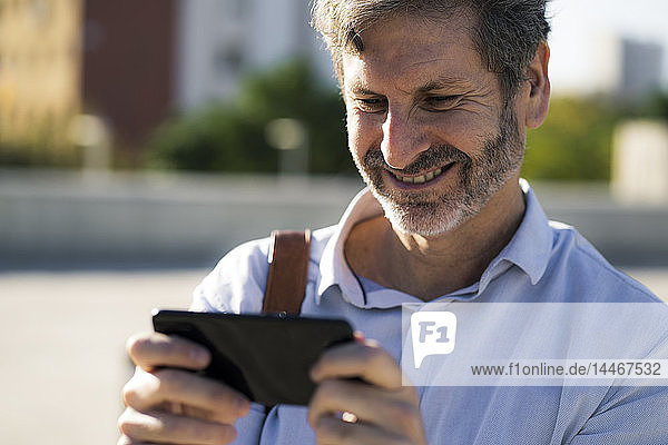 Lächelnder reifer Mann  der draußen auf sein Handy schaut