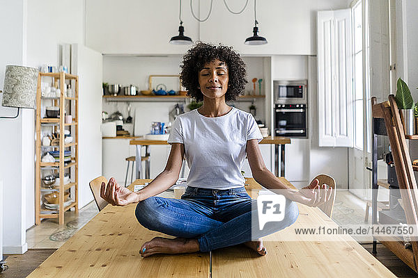 Lächelnde Frau mit geschlossenen Augen in Yoga-Pose auf Tisch zu Hause