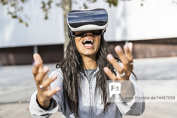 Junge Frau  die in der Stadt eine VR-Brille trägt und die Hand ausstreckt